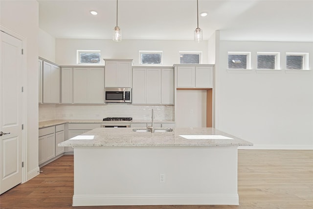 kitchen featuring a kitchen island with sink, pendant lighting, light stone countertops, and appliances with stainless steel finishes