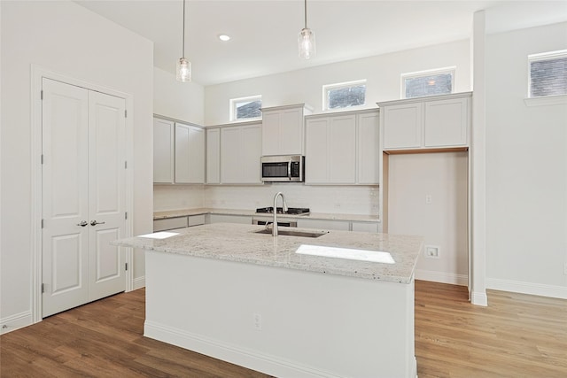 kitchen featuring light stone counters, light hardwood / wood-style floors, an island with sink, and hanging light fixtures