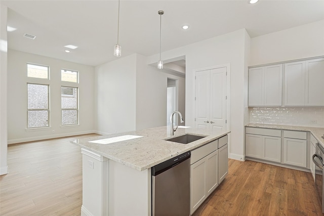 kitchen featuring sink, hanging light fixtures, stainless steel dishwasher, an island with sink, and decorative backsplash