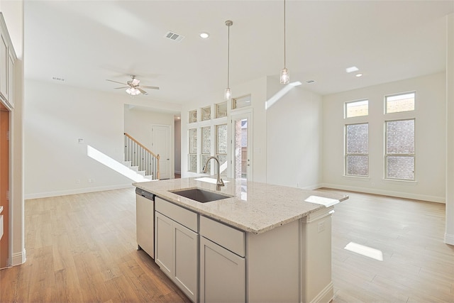 kitchen featuring light stone countertops, sink, pendant lighting, a center island with sink, and dishwasher