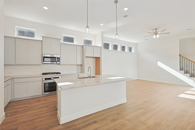 kitchen featuring light stone counters, stainless steel appliances, sink, pendant lighting, and an island with sink