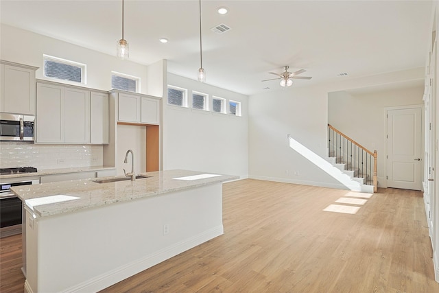 kitchen featuring sink, stainless steel appliances, light stone counters, pendant lighting, and a center island with sink