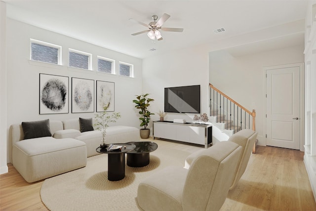 living room with a ceiling fan, visible vents, stairway, and light wood-style flooring