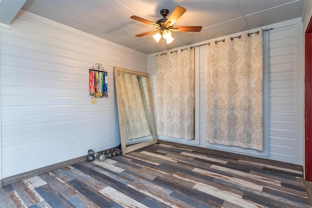 unfurnished room with dark wood-type flooring, ceiling fan, and wood walls