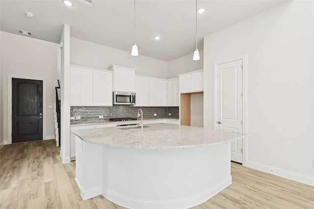 kitchen featuring white cabinets, light stone countertops, light wood-type flooring, and an island with sink