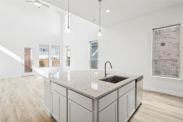 kitchen featuring a kitchen island with sink, sink, hanging light fixtures, and light wood-type flooring