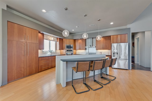 kitchen with a center island, a kitchen breakfast bar, light wood-type flooring, appliances with stainless steel finishes, and decorative light fixtures