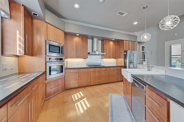 kitchen with decorative backsplash, appliances with stainless steel finishes, wall chimney exhaust hood, sink, and decorative light fixtures