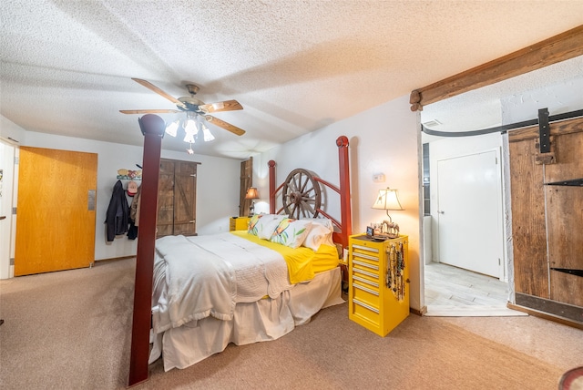 bedroom with light colored carpet, a textured ceiling, ceiling fan, and a barn door