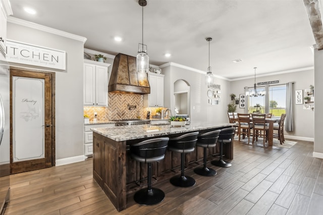 kitchen featuring white cabinets, premium range hood, a large island, dark wood-type flooring, and light stone countertops