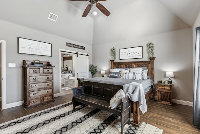 bedroom with a barn door, connected bathroom, dark hardwood / wood-style flooring, and ceiling fan