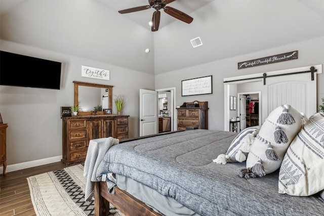 bedroom featuring a spacious closet, dark wood-type flooring, a barn door, a closet, and ceiling fan