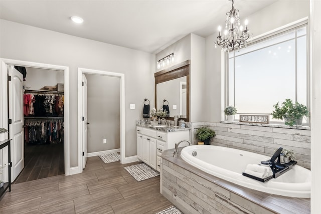 bathroom with tiled bath, vanity, and an inviting chandelier