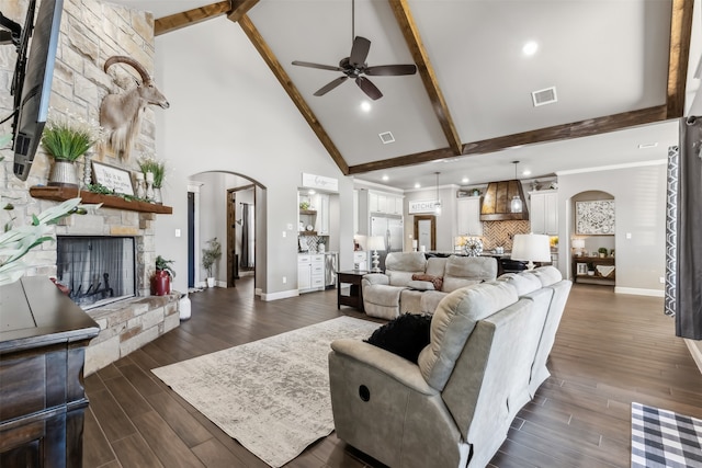 living room with dark hardwood / wood-style flooring, beamed ceiling, high vaulted ceiling, a stone fireplace, and ceiling fan