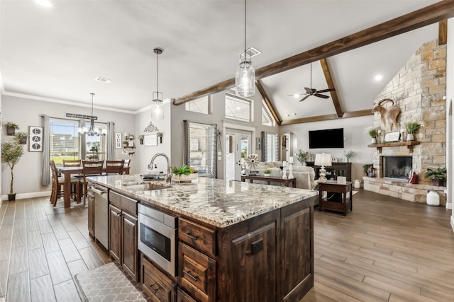 kitchen with light stone counters, sink, wood-type flooring, a stone fireplace, and a kitchen island with sink