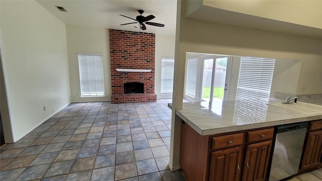 kitchen featuring a fireplace, dishwasher, tile countertops, sink, and ceiling fan