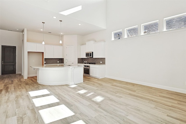 kitchen with a kitchen island with sink, white cabinets, a towering ceiling, light hardwood / wood-style floors, and stainless steel appliances