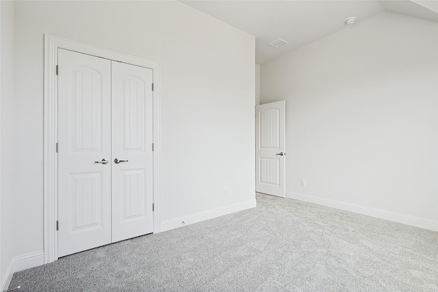 unfurnished bedroom featuring light colored carpet, vaulted ceiling, and a closet