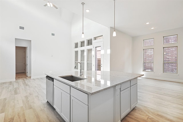 kitchen featuring sink, light stone counters, hanging light fixtures, stainless steel dishwasher, and a kitchen island with sink