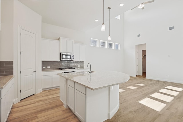 kitchen with a center island with sink, white cabinetry, appliances with stainless steel finishes, and tasteful backsplash