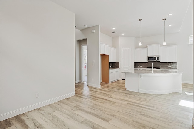 kitchen with pendant lighting, a center island with sink, decorative backsplash, light wood-type flooring, and white cabinetry