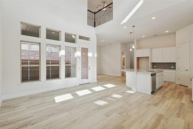 kitchen with pendant lighting, a high ceiling, a center island with sink, white cabinets, and stainless steel dishwasher