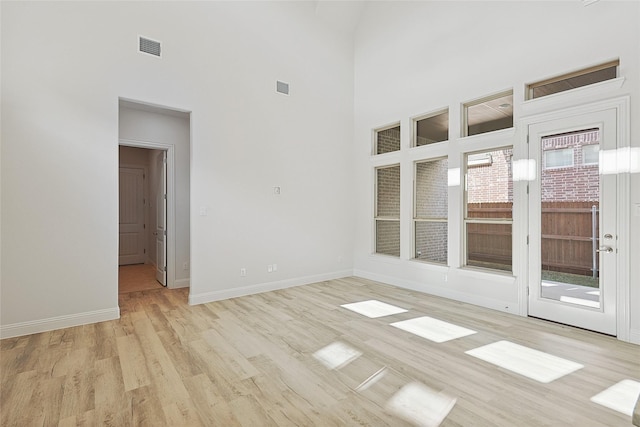 unfurnished room with light hardwood / wood-style flooring and a towering ceiling