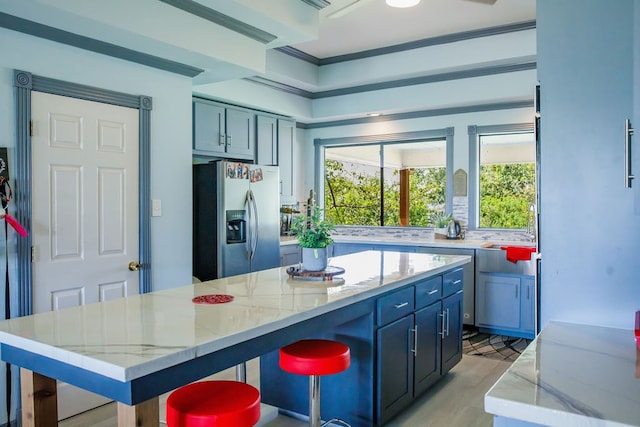 kitchen featuring a kitchen island, a breakfast bar area, stainless steel fridge, light stone countertops, and light hardwood / wood-style flooring