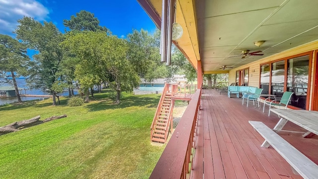 wooden terrace featuring a water view, a lawn, and ceiling fan