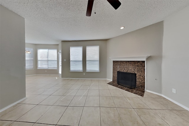 unfurnished living room with light tile patterned floors, ceiling fan, a tile fireplace, and a textured ceiling