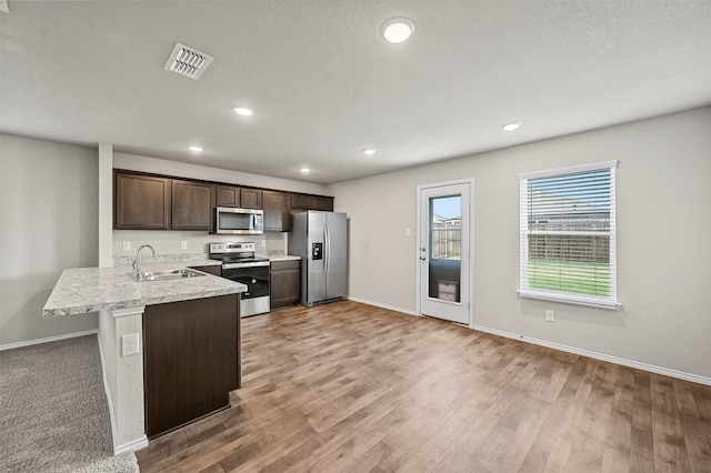 kitchen with light wood-type flooring, appliances with stainless steel finishes, kitchen peninsula, and sink