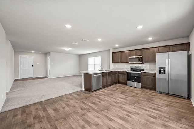 kitchen with light hardwood / wood-style flooring, stainless steel appliances, kitchen peninsula, sink, and dark brown cabinetry