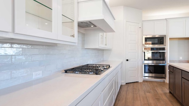 kitchen with tasteful backsplash, white cabinetry, stainless steel appliances, and custom exhaust hood