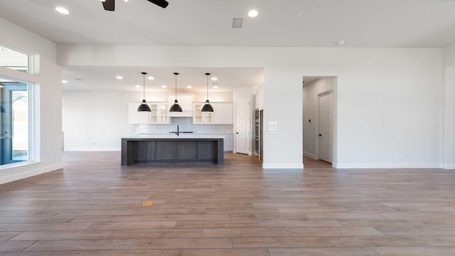 kitchen featuring decorative light fixtures, a healthy amount of sunlight, light hardwood / wood-style floors, and a kitchen island with sink