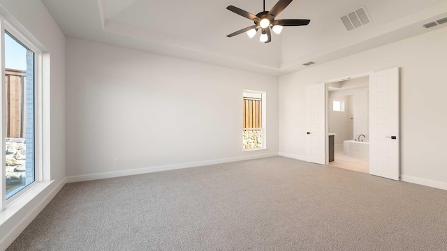 unfurnished bedroom featuring a raised ceiling, ensuite bath, ceiling fan, and light carpet