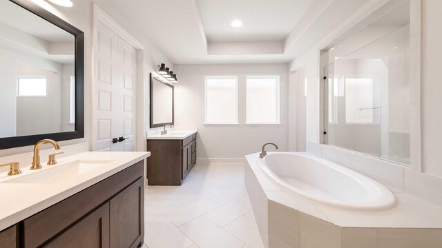 bathroom with tiled bath, vanity, a tray ceiling, and tile patterned floors