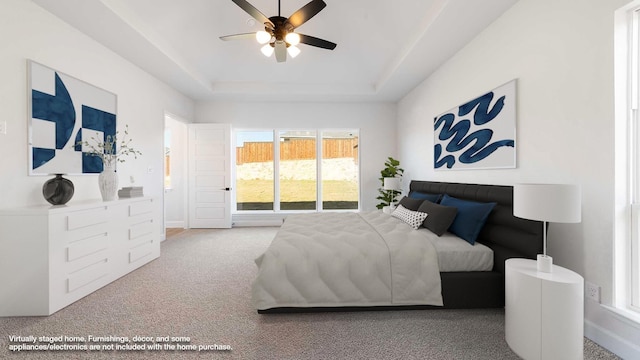 carpeted bedroom with a raised ceiling and ceiling fan