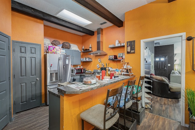 kitchen with beamed ceiling, kitchen peninsula, a kitchen breakfast bar, stainless steel refrigerator with ice dispenser, and wall chimney exhaust hood