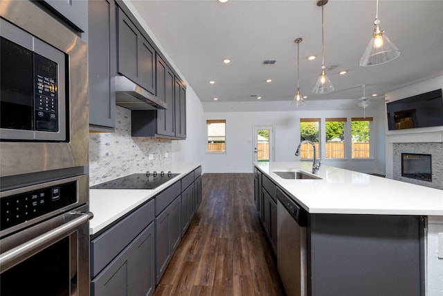 kitchen with dark wood-type flooring, sink, a center island with sink, stainless steel appliances, and decorative backsplash