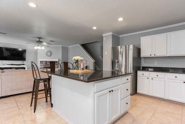 kitchen with a kitchen island, ceiling fan, stainless steel fridge, and white cabinetry