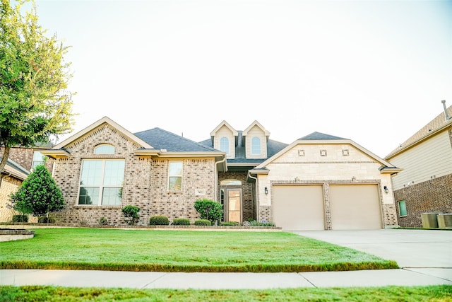 view of front of home featuring driveway, a front yard, a garage, brick siding, and central AC unit