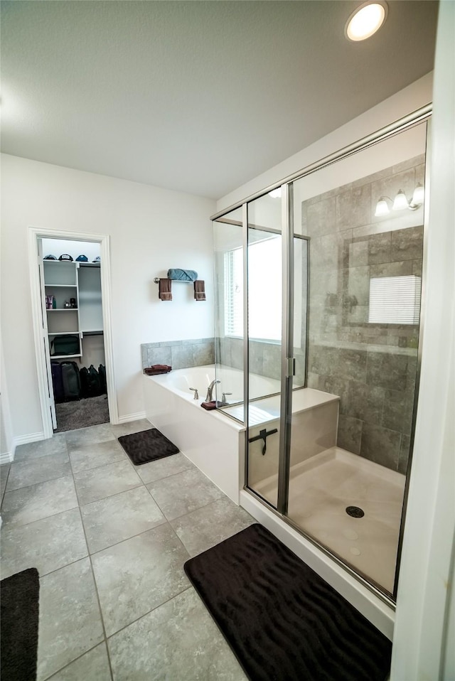 full bath with tile patterned floors, a walk in closet, a shower stall, baseboards, and a bath