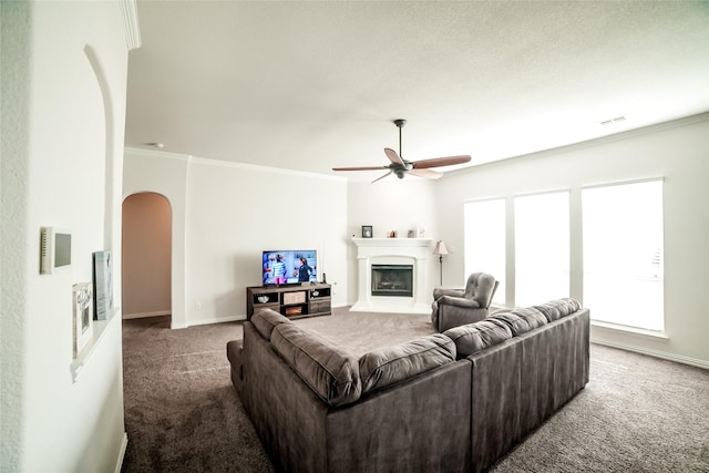 carpeted living area with visible vents, a large fireplace, arched walkways, crown molding, and baseboards