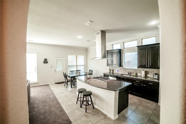 kitchen with tasteful backsplash, a kitchen island, dark stone counters, a kitchen bar, and island range hood