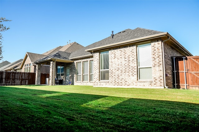 back of property with a yard, brick siding, a shingled roof, and fence