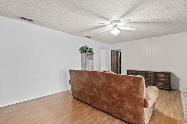 living room with ceiling fan, a textured ceiling, and light hardwood / wood-style flooring