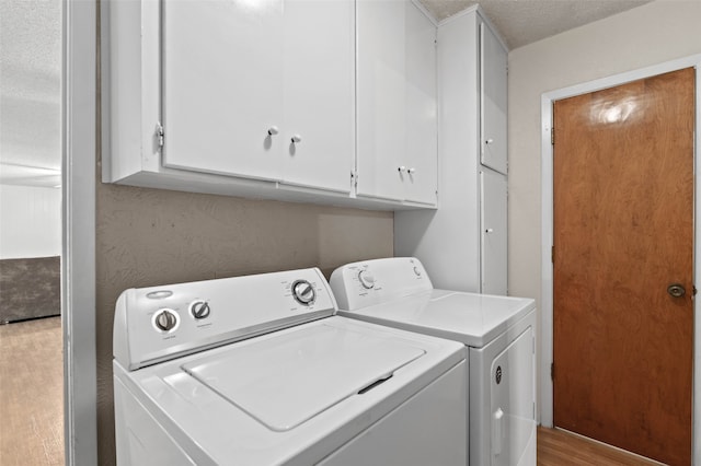 laundry room featuring a textured ceiling, light hardwood / wood-style floors, cabinets, and washer and dryer