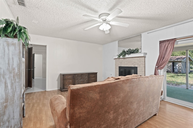 living room with light hardwood / wood-style flooring, ceiling fan, a textured ceiling, and a brick fireplace