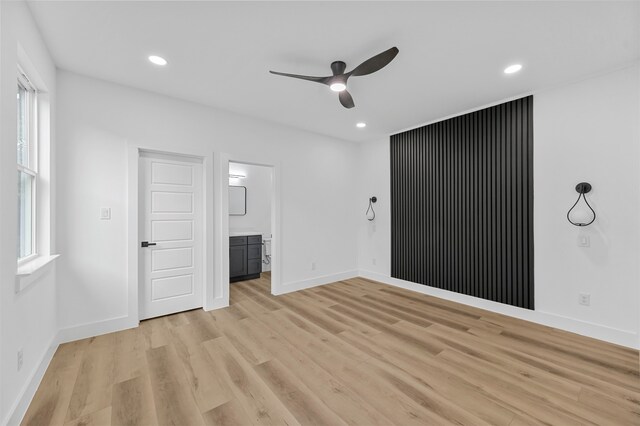 unfurnished bedroom with ensuite bathroom, ceiling fan, light wood-type flooring, and multiple windows