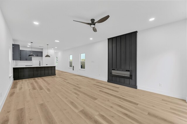 unfurnished living room featuring light hardwood / wood-style flooring, sink, and ceiling fan